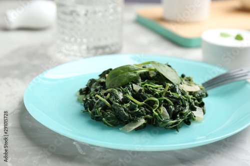 Plate with cooked spinach and fork on grey table, closeup. Healthy food photo