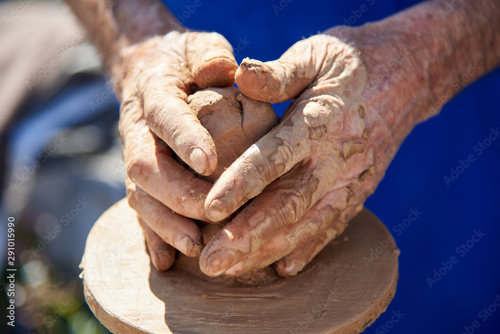 Hands of the grandfather who makes a clay pot on the machine.