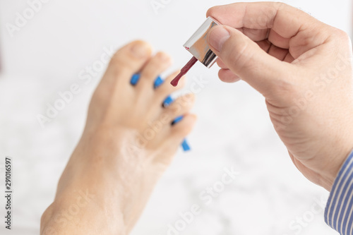 male hand holding a nail polish brush for painting a female barefoot