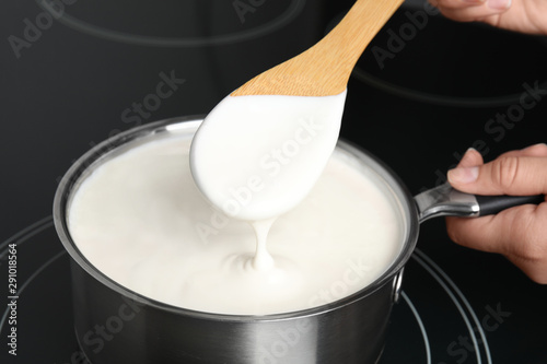 Woman cooking delicious creamy sauce in pan on stove, closeup