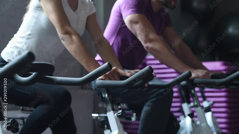 Attractive woman and man biking in the gym, exercising legs doing cardio workout cycling bikes. Couple in a spinning class wearing sportswear. Fitness healthy lifestyle concept Attractive woman and man biking in the gym, exercising legs doing cardio workout cycling bikes. Couple in a spinning class wearing sportswear. Fitness healthy lifestyle concept