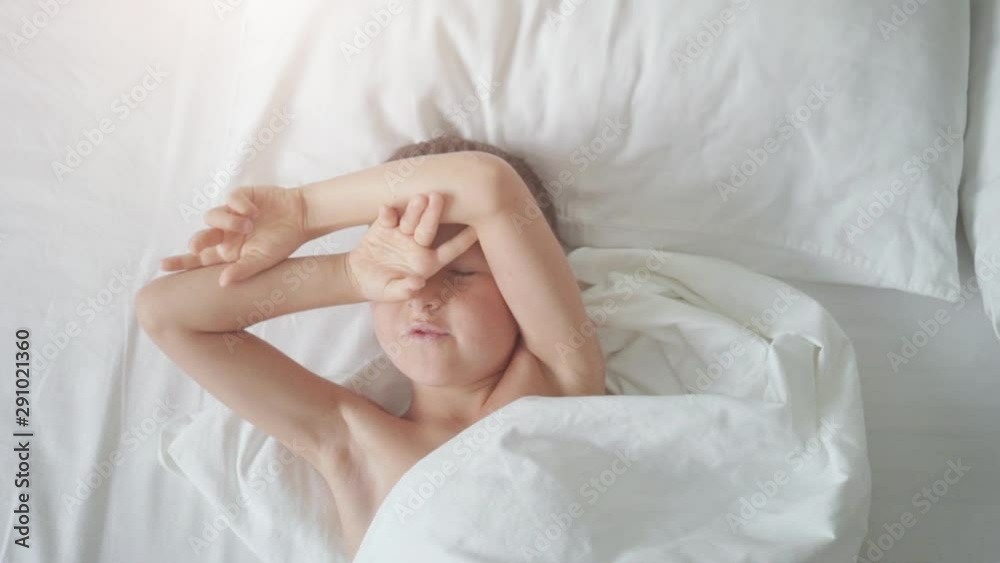 Top view of a young boy yawning and stretching arms in bed Top view of a young boy yawning and stretching arms in bed