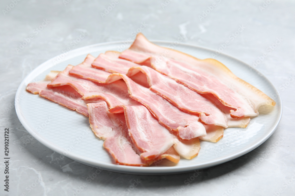 Plate of sliced raw bacon on light grey marble table
