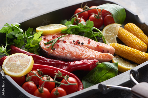 raw salmon steak with spices, vegetables and greenery in grill pan