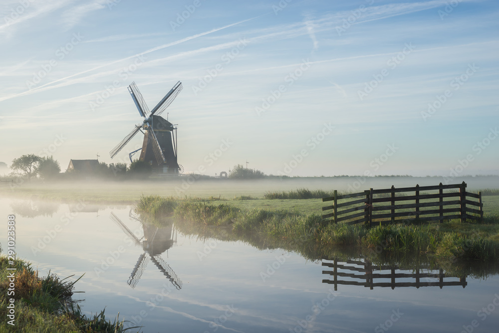 Classic dutch windmill along the water of a canal in the polder landscape of Holland with fogbanks over the fields