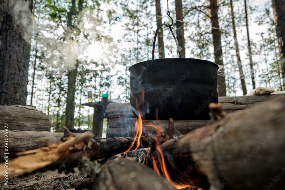 Black bowlers over a fire in the forest. Summer camp tourists. Time for preparing dinner Black bowlers over a fire in the forest. Summer camp tourists. Time for preparing dinner