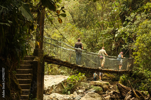 During a walk through the rainforest, tourists cross a suspension bridge over a river in the Cocora Valley, between the mountains of the Cordillera Central in Colombia. photo