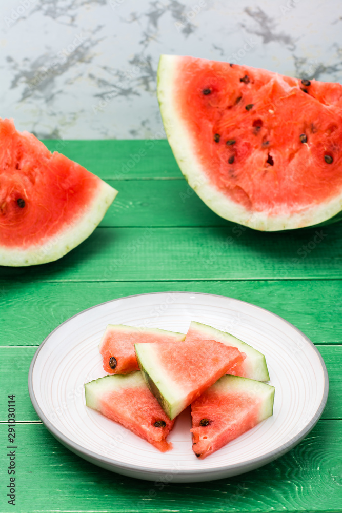 Sliced watermelon on a plate and uncut watermelon on a green wooden table Sliced watermelon on a plate and uncut watermelon on a green wooden table