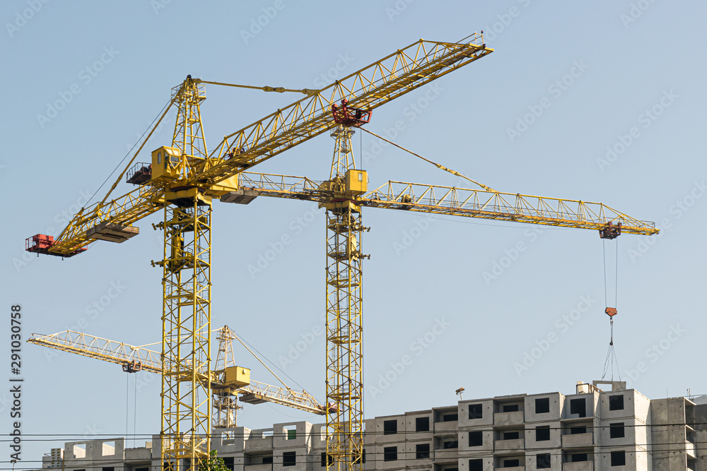 Several yellow high-rise construction cranes build multi-storey multi-apartment residential buildings using modern technologies of metal, concrete and brick according to the architectural design