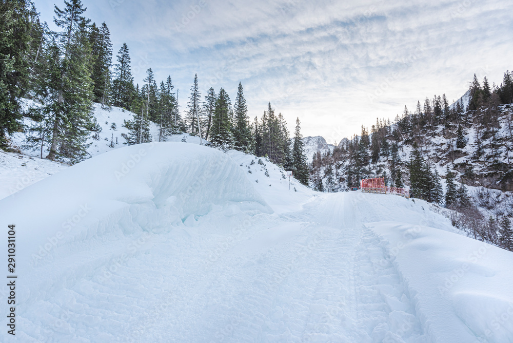 Snowcovered mountain road in a winter scenery with snowdrifts and snowy forest Snowcovered mountain road in a winter scenery with snowdrifts and snowy forest