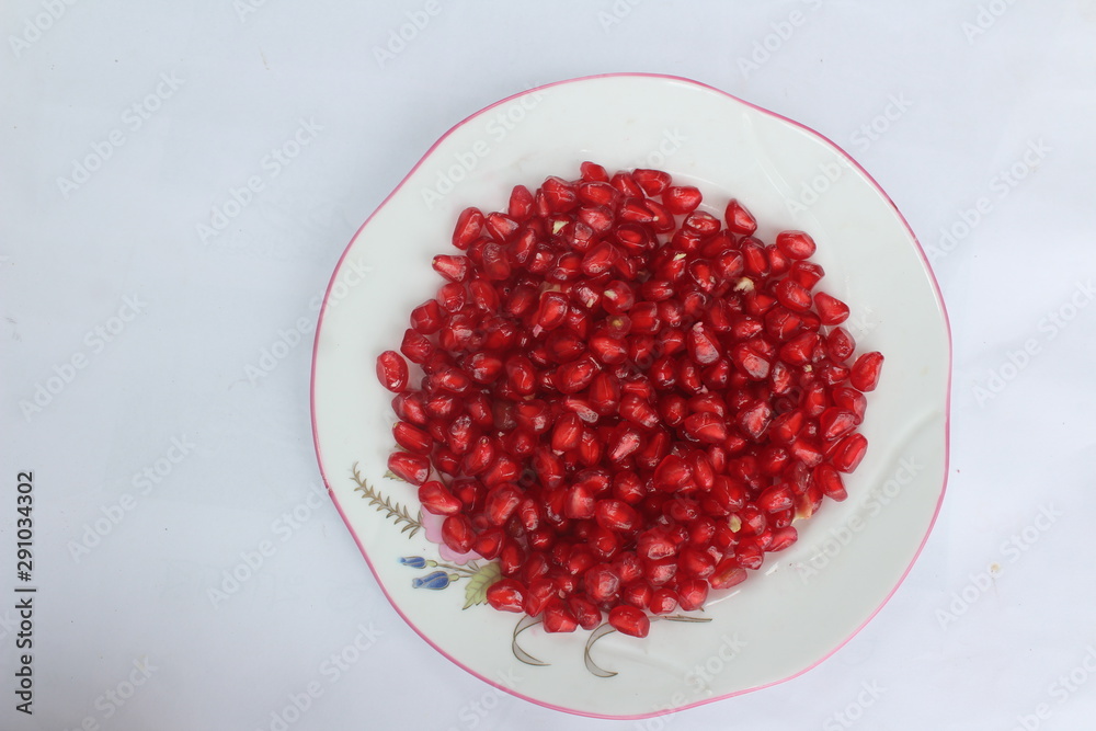 Pomegranate seeds placed in a plate with scattered seeds on white background Pomegranate seeds placed in a plate with scattered seeds on white background
