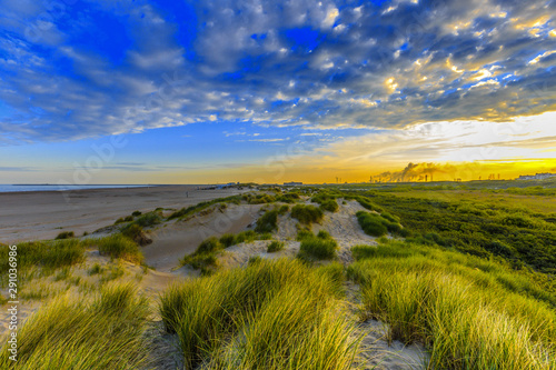Fototapeta Naklejka Na Ścianę i Meble -  Landscape with sea and dunes at IJmuiden with backgrounds of chimneys with smoke blasts of the blast furnaces in Velsen at sunrise