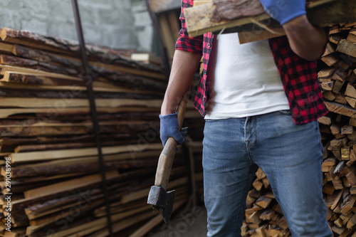 A man with an ax and firewood in his hands stands on the background of blanks for the winter