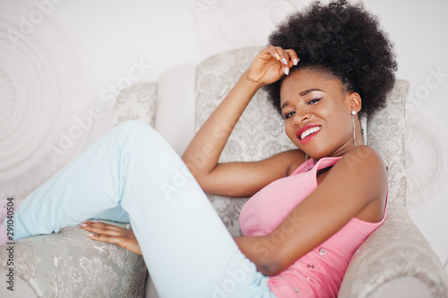 Young african american woman in pink singlet sitting on chair against white wall.