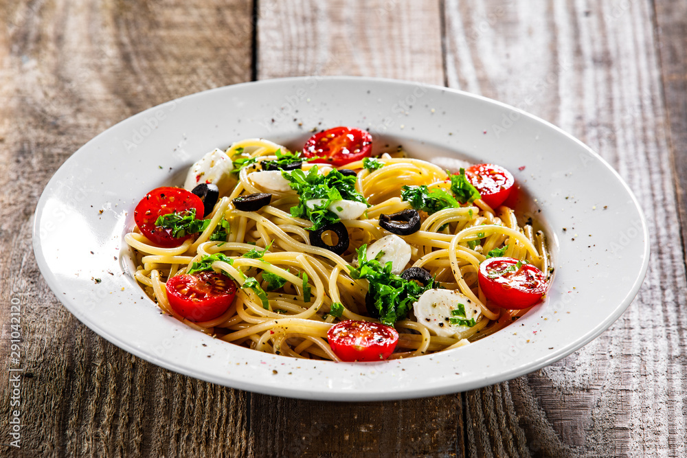 Pasta with cherry tomatoes and mozzarella cheese on wooden table Pasta with cherry tomatoes and mozzarella cheese on wooden table