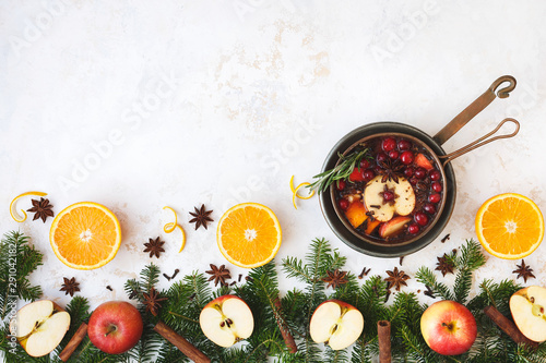 Mulled wine in copper saucepan cooked with slices of orange, apple , cranberries and spices. Golden white festive rustic surface. Top view, blank space