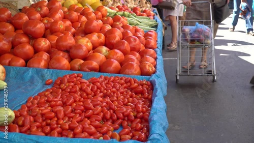 Beautiful tomatoes displayed in street market and people passing by. Handheld photo
