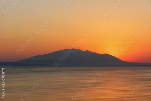 Burning Nea Vrasna sunrise in Greece. The Sun is rising behind the mountains and throwing first light at sea.