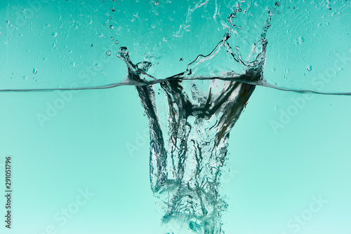 clear ice cubes falling deep in water with splash on turquoise background