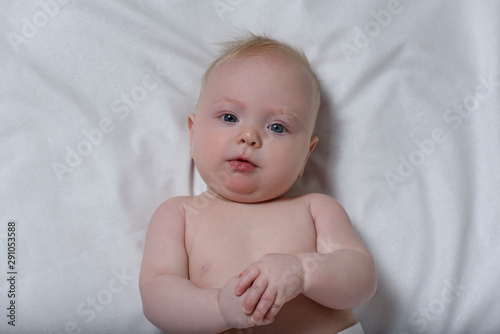 Portrait of a cute blond baby on a white sheet. Top view