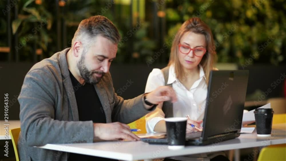 Couple of Coworkers Working Together at Office. Two Business Worker Preparing New Project on Laptop. They Write Down the Details in a Notebook.