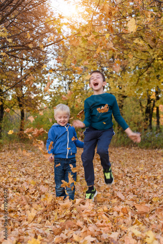 Two boys have fun, toss up leaves and jump in the park. Autumn day