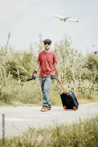 Traveler walking around with a camera in his hand and a backpack. There is a plane in the sky photo