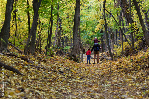 Father and two sons walking in the autumn forest. Younger son sitting on his father's shoulders. Back view