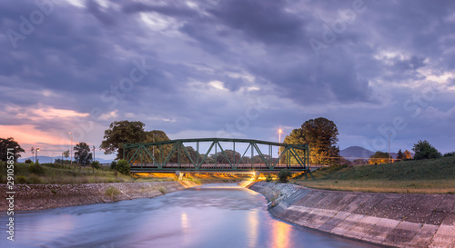 Lighten, iconic, metal railroad bridge in Pirot, Serbia, over silky water river Nisava and dramatic sunset sky