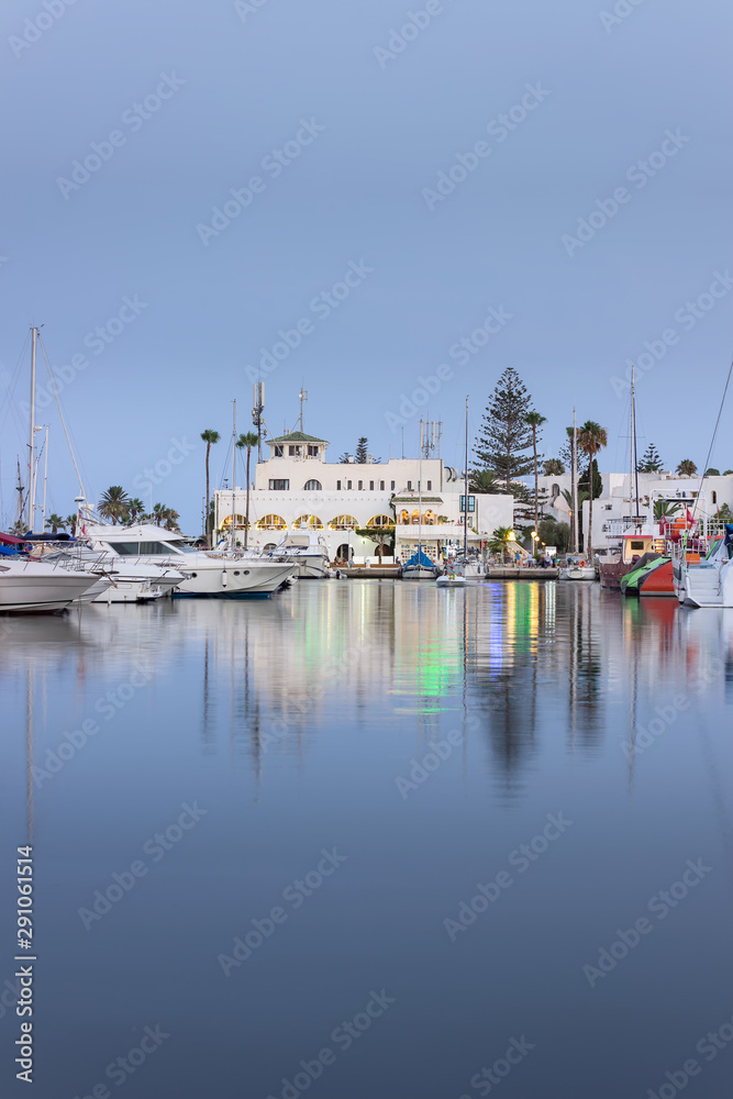 Blue hour at marina Port El Kantaoui, beautiful boats, yachts and ships parked in the reflective sea, restaurants and gift shops