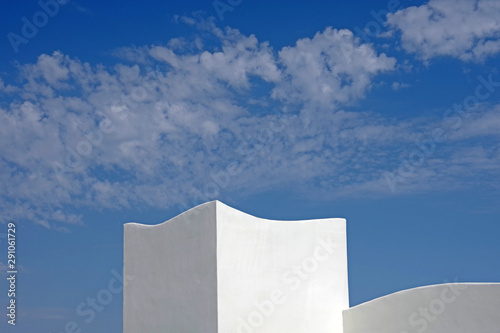 A close sectional view of the top of a white building with a deep blue sky with some white clouds above