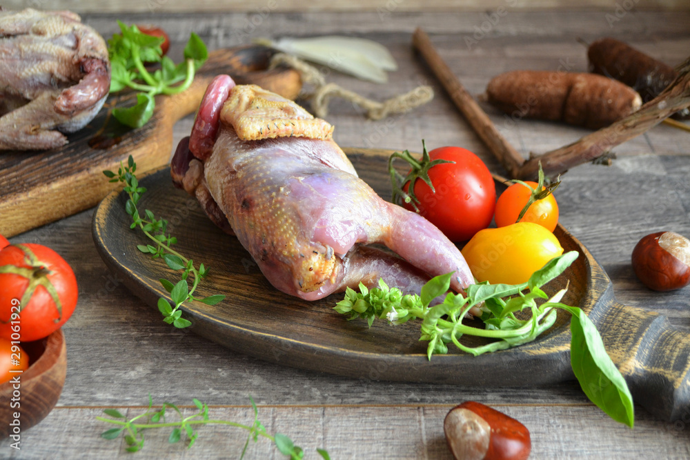 Fresh raw fowl partridge and ingredients in wooden plate on the dark kitchen table Fresh raw fowl partridge and ingredients in wooden plate on the dark kitchen table