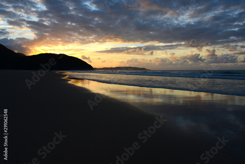 empty beach in Portugals Algarve with reflecting clouds in wet sand during sunset