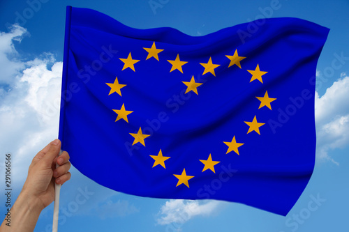 male hand holds against the background of the sky with clouds the national flag of the European Union on a luxury satin texture, silk with waves, closeup, copy space