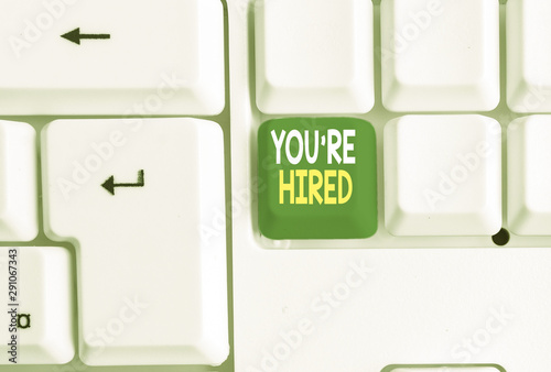 Conceptual hand writing showing You Re Hired. Concept meaning New Job Employed Newbie Enlisted Accepted Recruited White pc keyboard with note paper above the white background photo