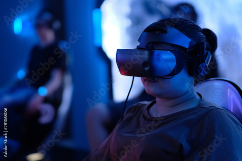close up one young female wearing VR headset watching movie. Blur people sitting on chair experience VR under blue lights