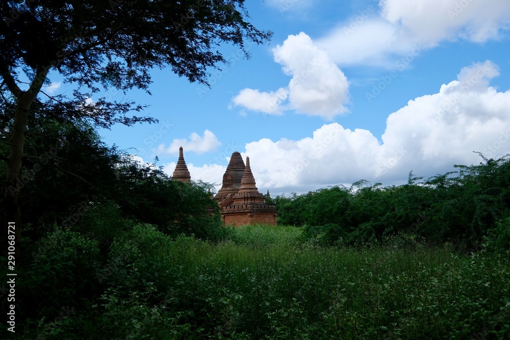 distant view of several ancient pagodas under blue sky white clouds. Green grass and trees foreground.In Bagan Myanmar distant view of several ancient pagodas under blue sky white clouds. Green grass and trees foreground.In Bagan Myanmar