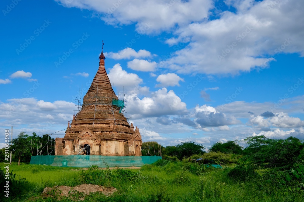 one damaged ancient pagoda is surrounded by scaffolding in Bagan Myanmar. Protect culture and history concept. Green plants around. Blue sunny sky white clouds