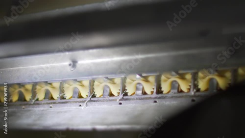 Closeup slow motion of organic pasta butterfly macaroni jumping out of the die of an automated pasta machine in a pasta factory. Food industry. photo