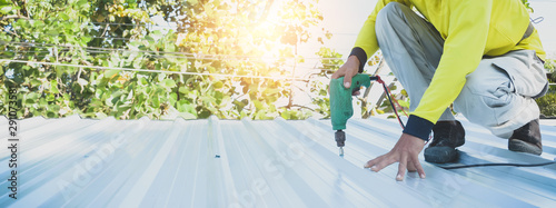 Roofers are using an electric drill to fire screws to assemble the metal sheets. For building the roof of the garage.