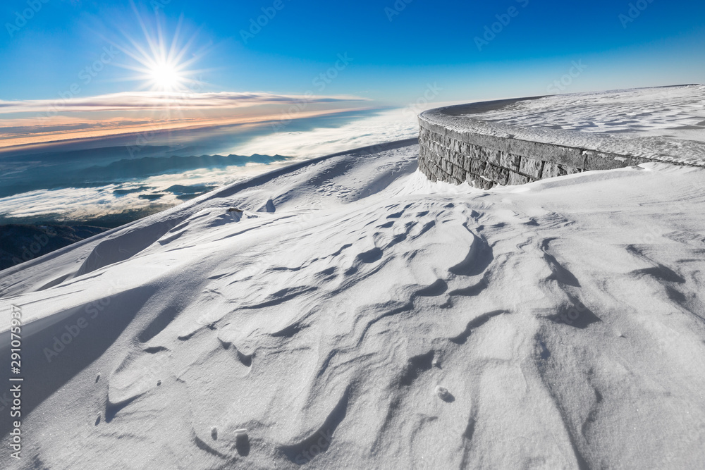 Low angle shot of a snow covered winter landscape at sunrise, with an embankment on the right and low clouds in the distance