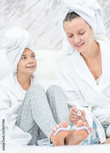 Happy family at home. Mother and daughter are doing pedicures. Mom and child girl are in bathrobes and with towels on their heads