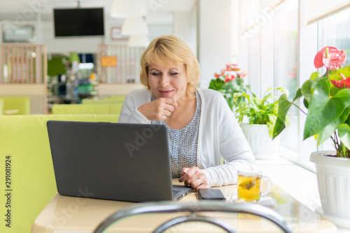 A woman with a laptop looks at a document in a cafe, office