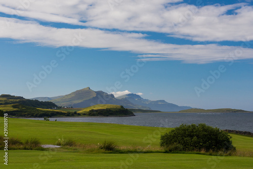 Peaceful and iconic landscape of the scottish Skye island, with a green meadow in foreground and distant mountains in the background