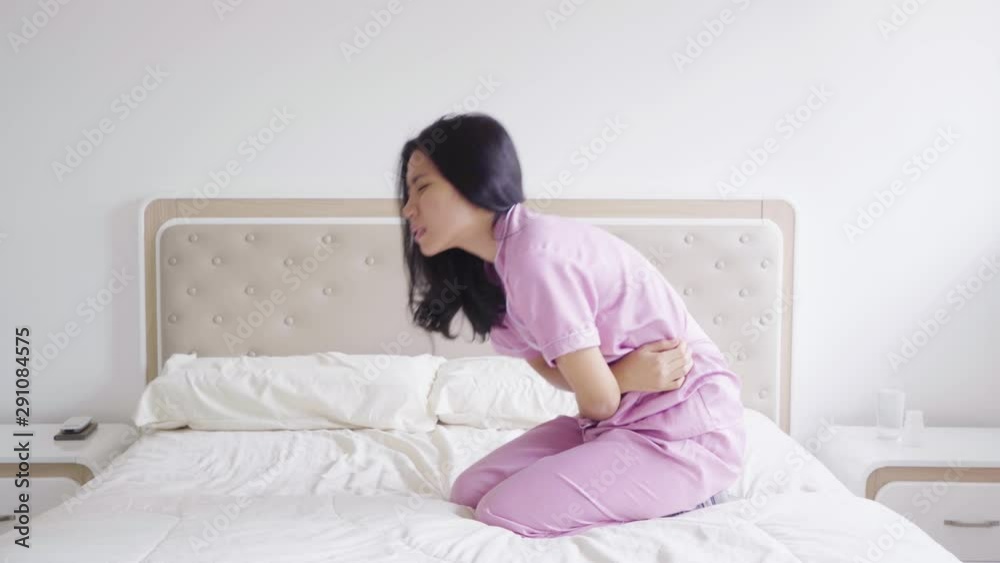 Young woman having stomach ache or abdominal cramp during menstruation period in the bedroom at home. Shot in 4k resolution Young woman having stomach ache or abdominal cramp during menstruation period in the bedroom at home. Shot in 4k resolution