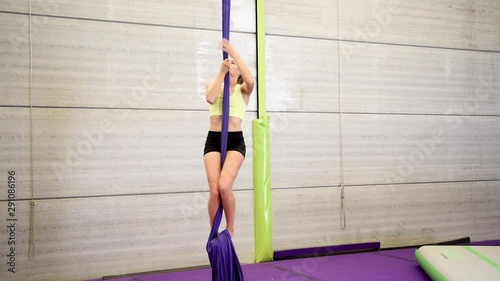 Young redheaded woman doing aerial gymnastic acrobatics with acrobatic fabrics inside a gym.
