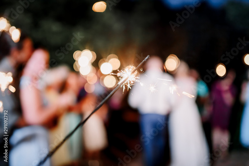 A crowd of young happy people with sparklers in their hands during celebration. Sparkler in hands on a wedding - bride, groom and guests holding lights in hand. Sparkling lights of bengal fires.