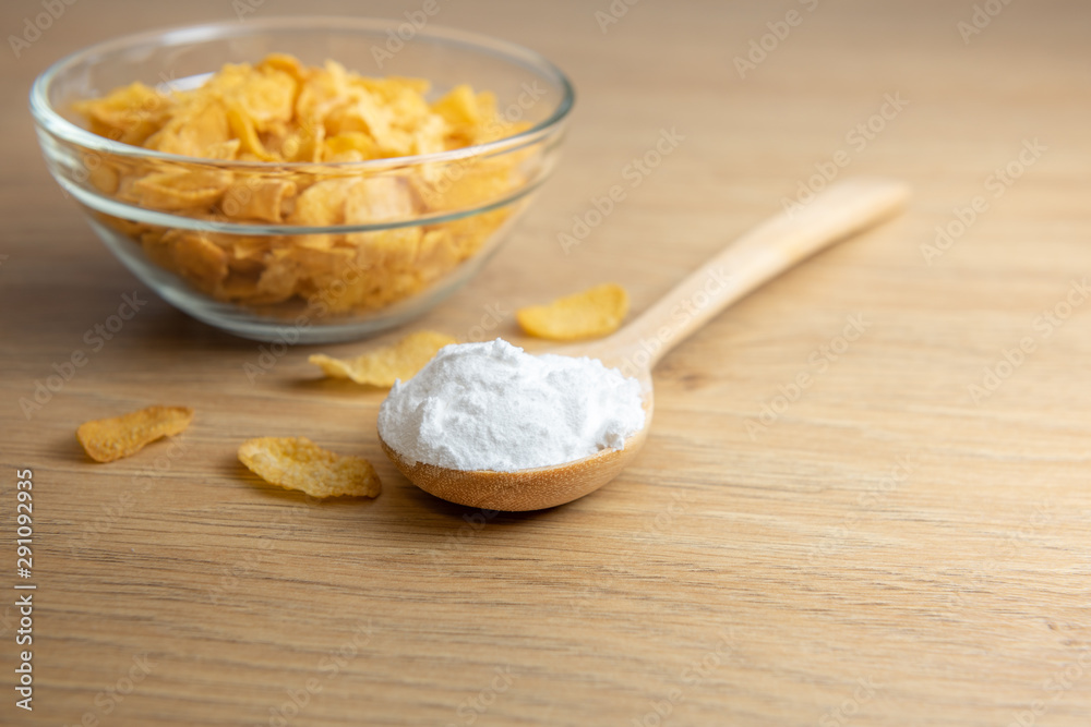 Close-up of starch or flour powder in wooden spoon with cornflakes on wooden background Close-up of starch or flour powder in wooden spoon with cornflakes on wooden background