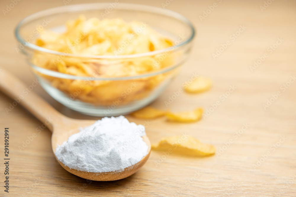 Close-up of starch or flour powder in wooden spoon with cornflakes on wooden background Close-up of starch or flour powder in wooden spoon with cornflakes on wooden background