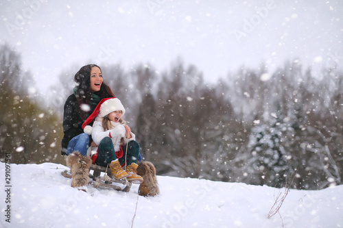 A winter fairy tale, a young mother and daughter in the forest. A girl on a sled with gifts on the eve of the new year in the park. Two sisters walk in a New Year's park and ride a sled with gifts.